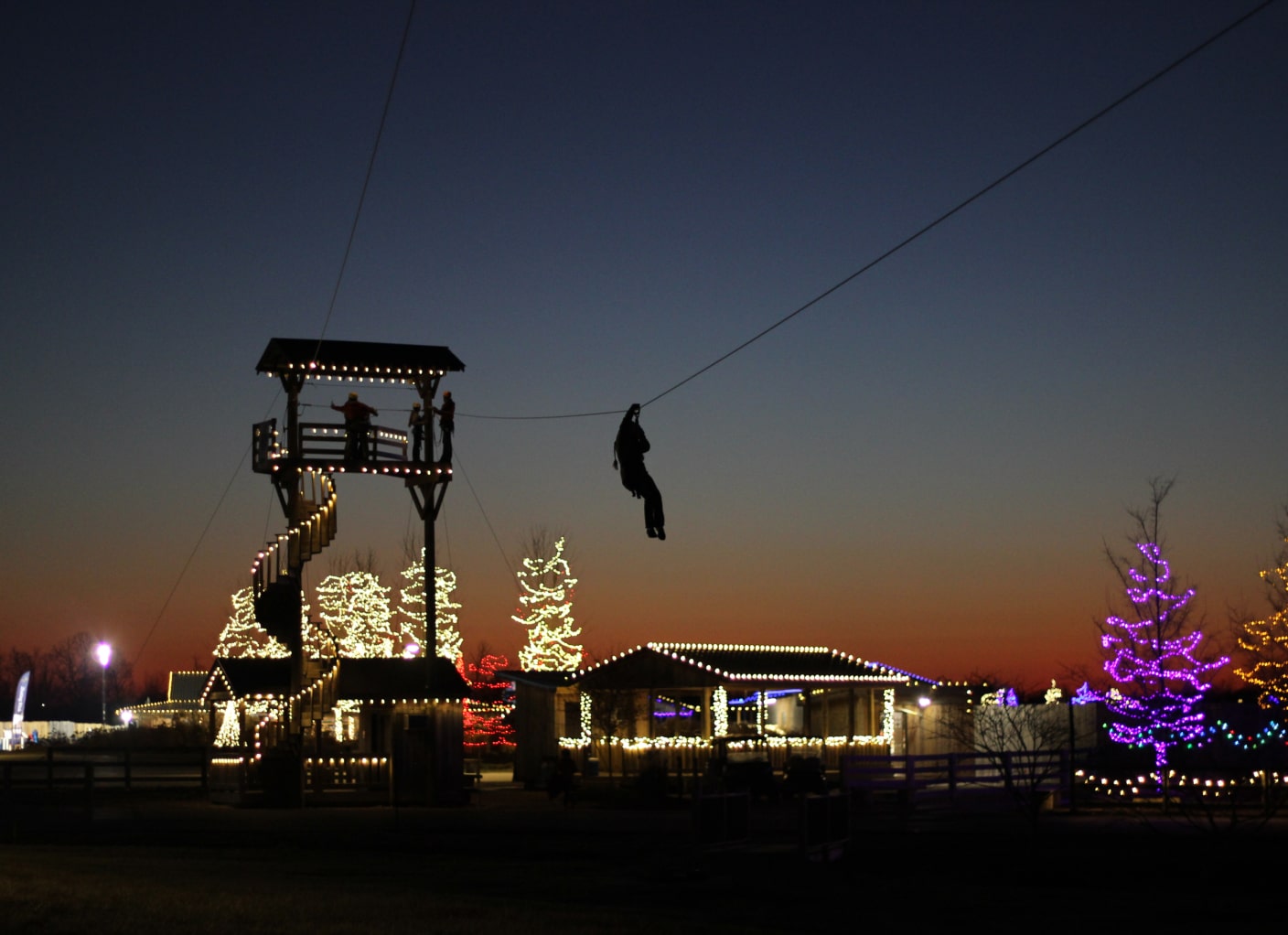 person ziplining during christmas time lights at the ark